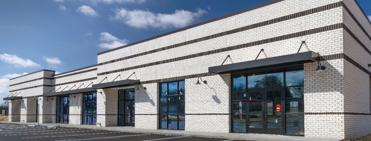 A long white brick buildinf with black brick accents. It has black trimmed window and doors.